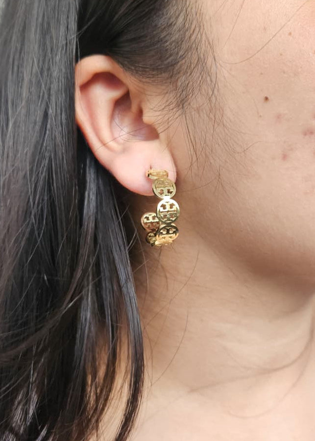 Gold heart-shaped earrings worn by a person with dark hair.