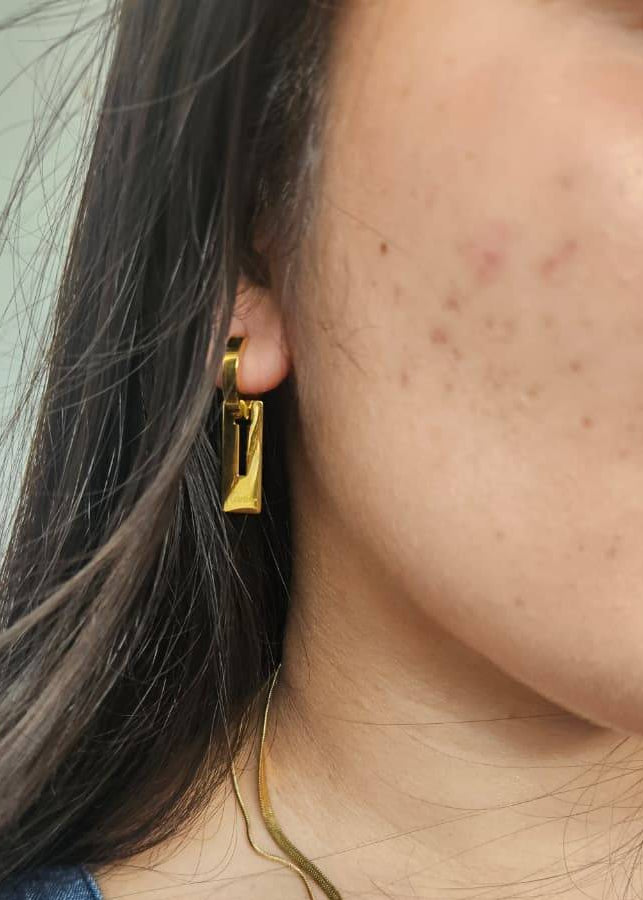 Close-up of a person wearing a gold earring with a neutral background