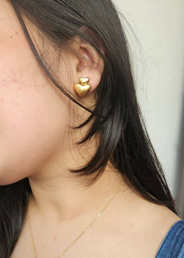 Close-up of a person wearing gold heart-shaped earrings.