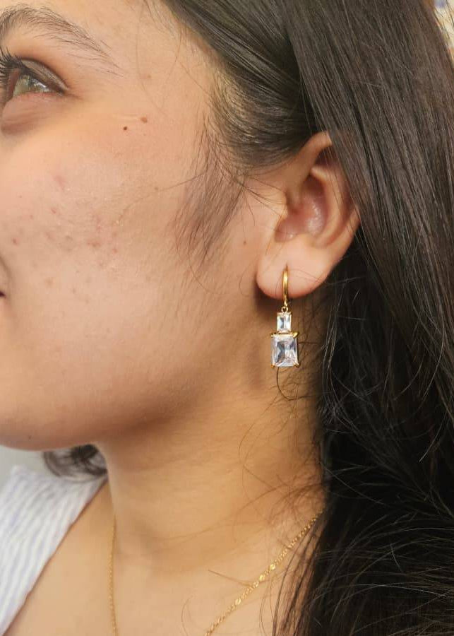 Close-up of a person wearing gold earrings with a clear gemstone.