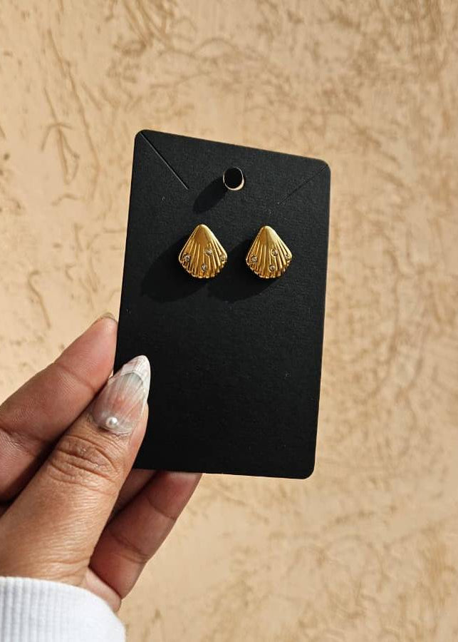 Gold shell-shaped earrings on a black card held by a hand against a beige background