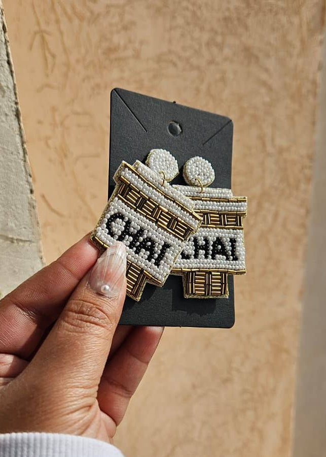 Earrings on a card held by a hand against a beige wall that says chai