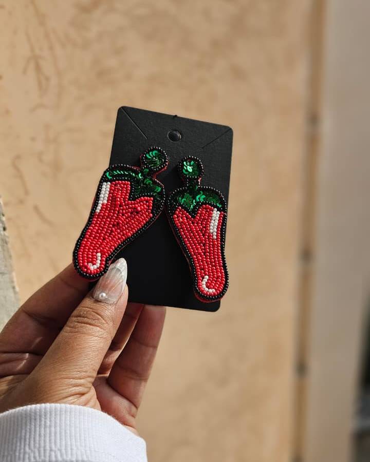 Pair of red chili pepper earrings on a black card held by a hand against a beige background