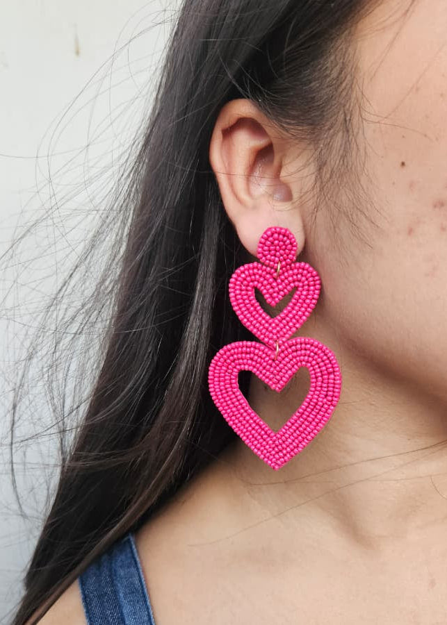 Close-up of a person wearing bright pink heart-shaped earrings against a neutral background