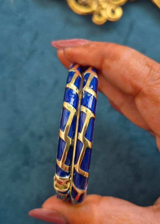 Hand holding a blue bangle with gold patterns against a teal background