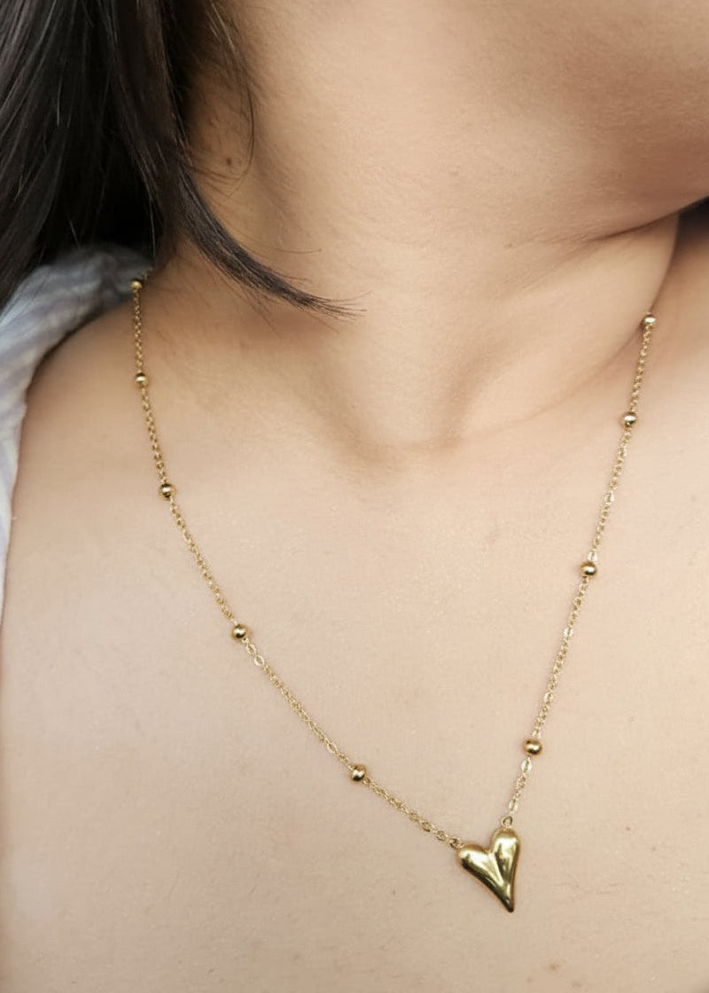 Gold necklace with a heart pendant worn by a person