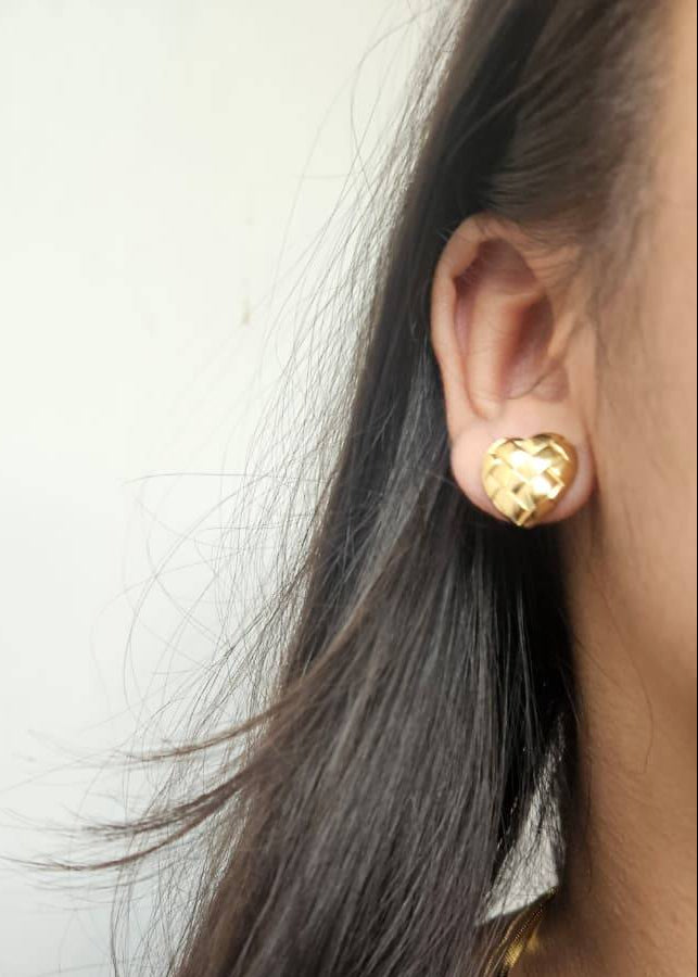 Close-up of a person wearing a gold earring with a plain background