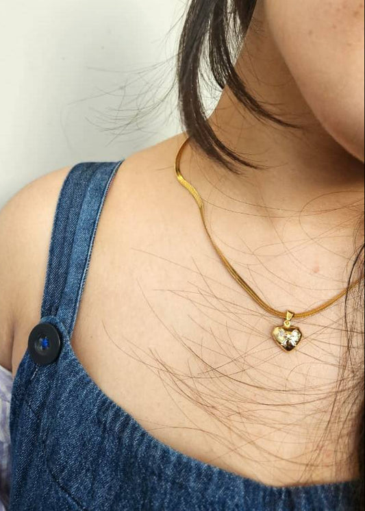 Person wearing a gold necklace with a heart pendant, close-up on neck and shoulder.