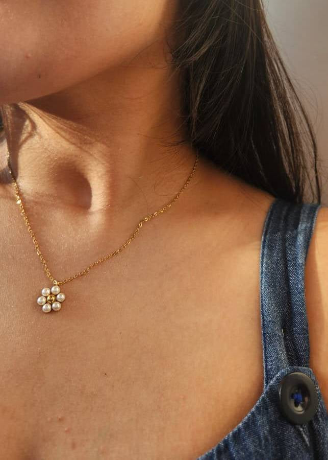 Close-up of a necklace with a floral pendant worn by a person in a denim outfit.