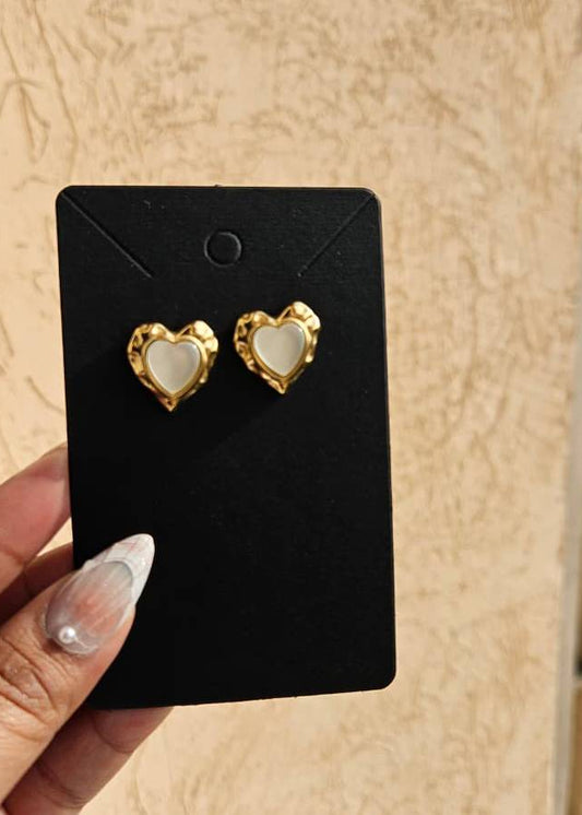 Heart-shaped earrings on a black card held by a hand with light nail polish.
