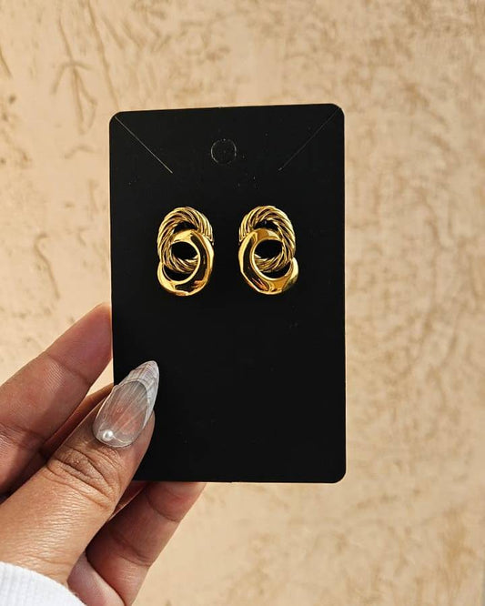Gold earrings on a black card held by a hand with beige nail polish against a beige background
