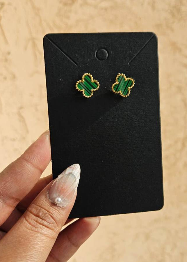 Clover-shaped earrings on a black card held by a hand against a beige background