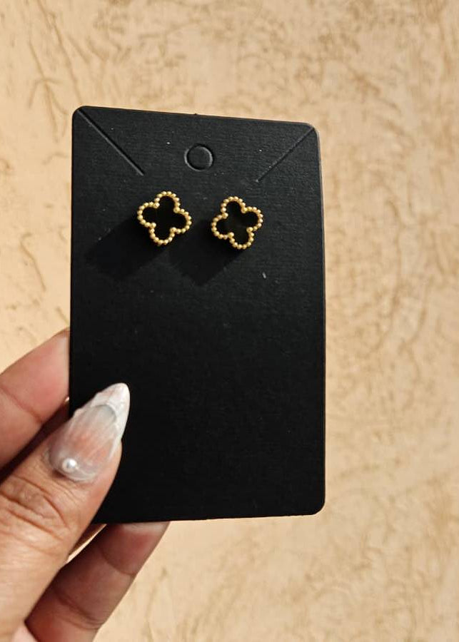 Gold earrings on a black card held by a hand against a beige background