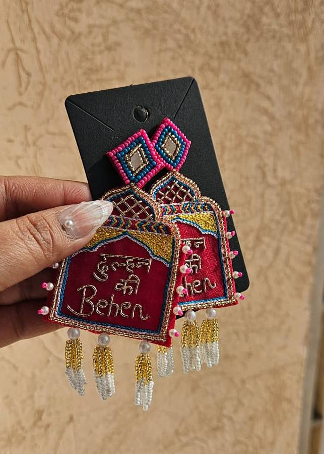 Decorative earring with intricate design and text held by a hand against a beige background