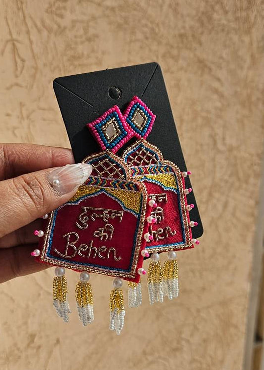 Decorative earring with intricate design and text held by a hand against a beige background
