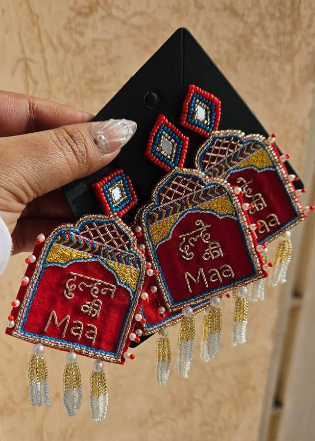 Decorative earrings with red and gold colors held by a hand against a beige background dulhe ki maa dulhan ki maa shadi haldi jewe