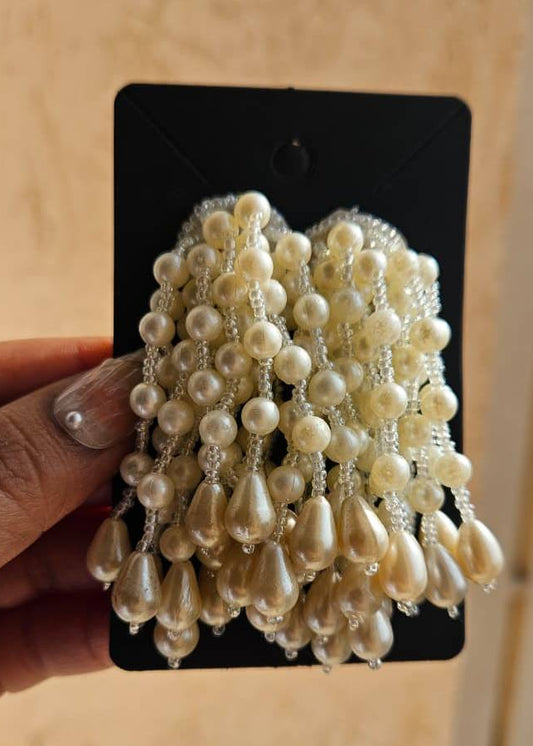 Pearl earrings on a black card held by a hand against a wooden background