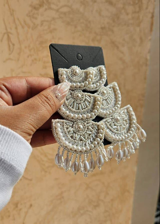 Hand holding a pair of decorative earrings on a beige background