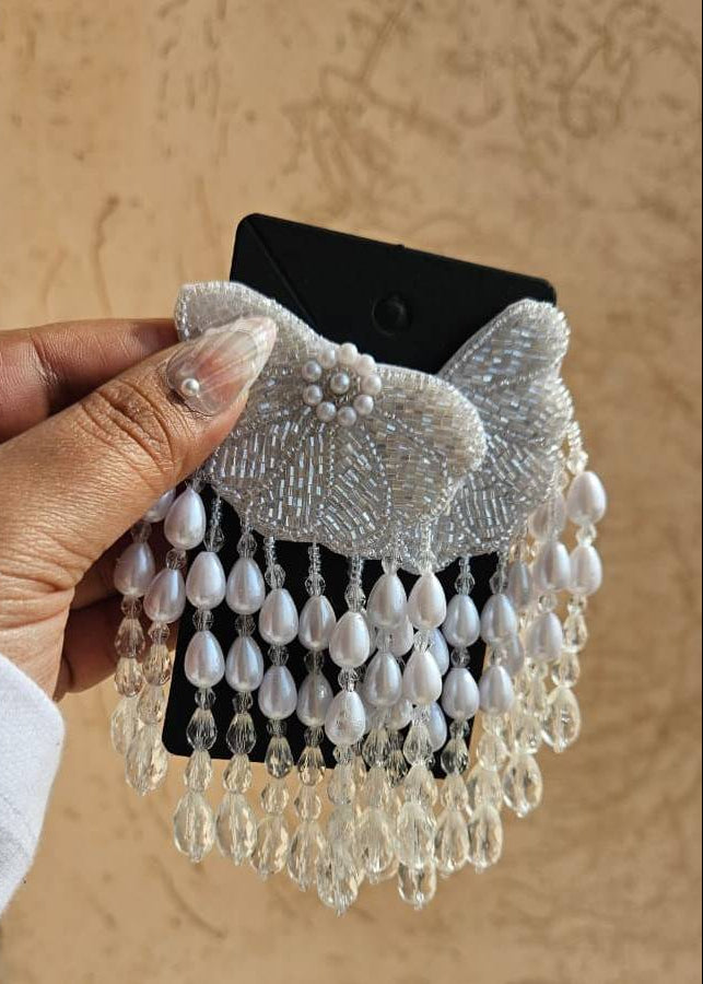 Hand holding a decorative Pearl Earring with beads against a beige wall.